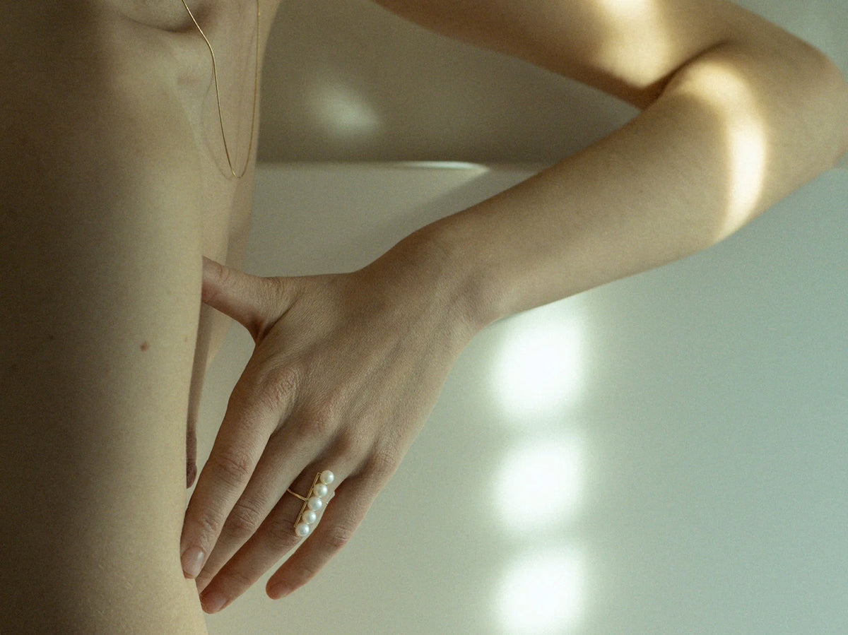 Editorial nude portrait of model in golden window light, hand on hip showing N 18 pearl ring