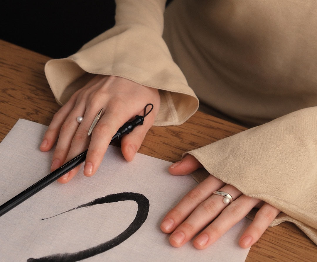 Hands resting on rice-paper script after calligraphy stroke, Gyosho ring detail visible