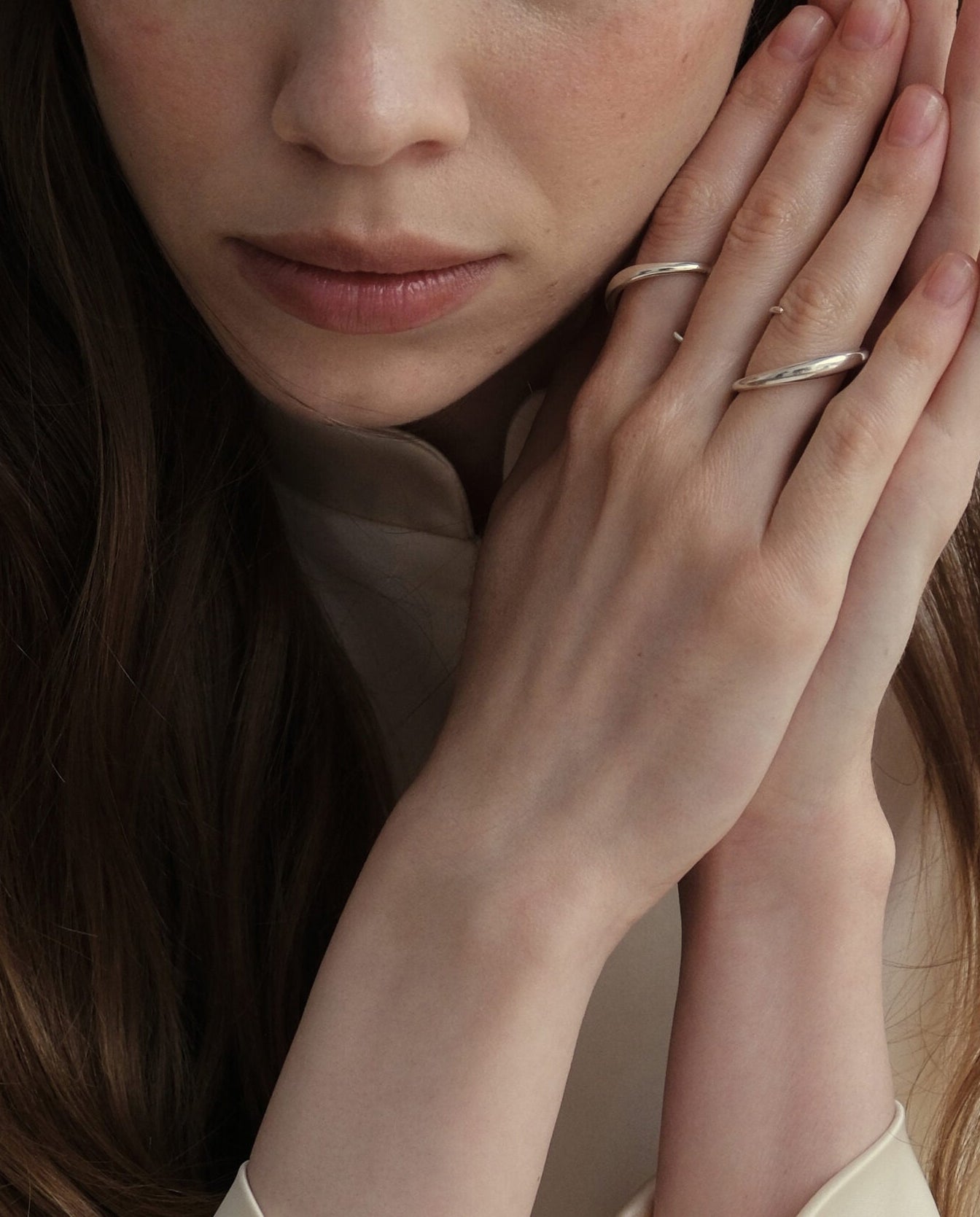 Model wearing Kaisho silver ring with other Lera Treyger bands, hands at face in soft cream styling