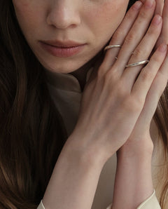 Model wearing Kaisho silver ring with other Lera Treyger bands, hands at face in soft cream styling