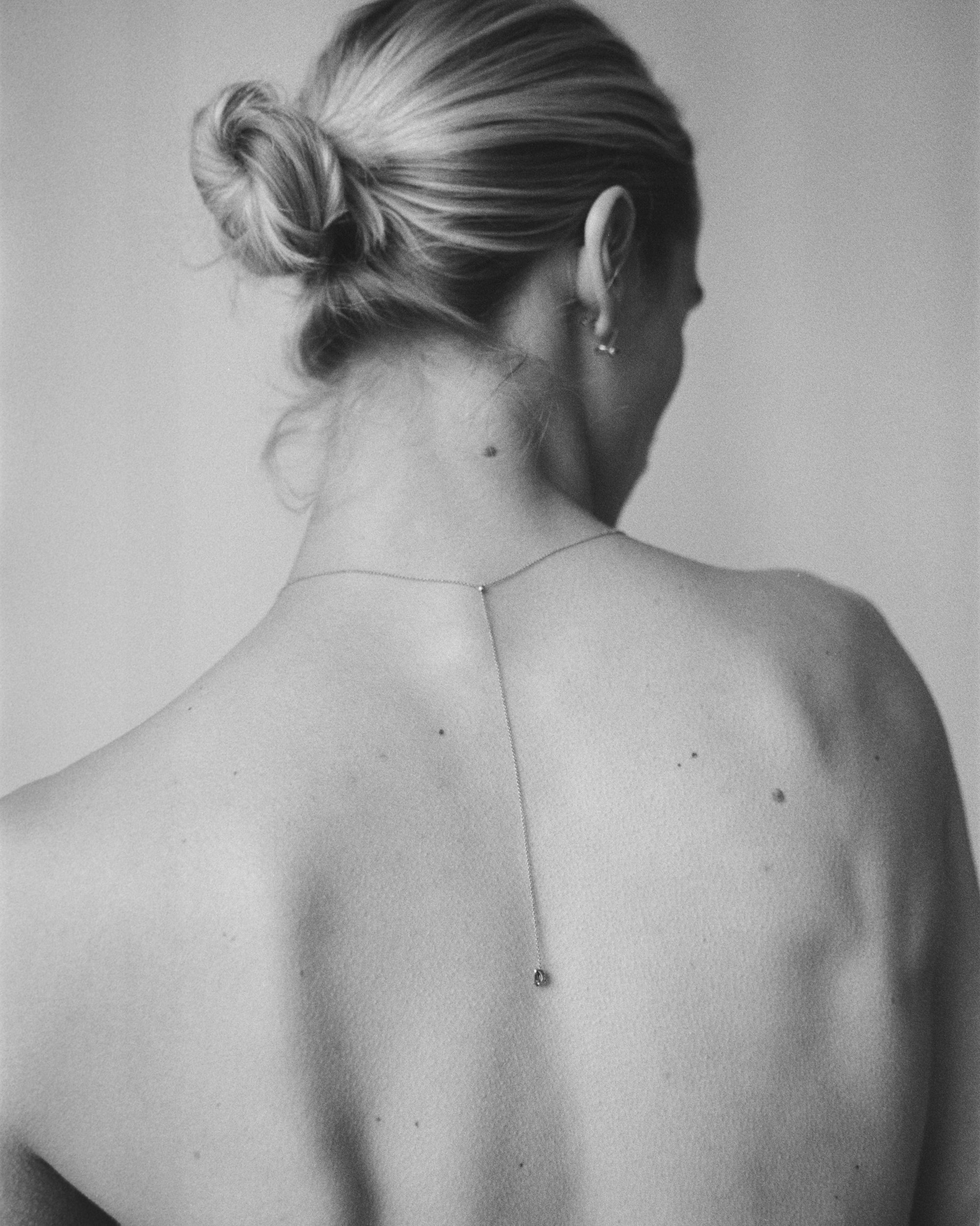 B&W rear view of blonde model with low bun wearing Lera Treyger MA 9 silver lariat down the bare spine