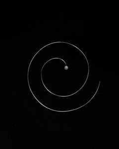 Atmospheric B&W still life of Lera Treyger Reisho sterling silver spiral hoop earring with central pearl on black