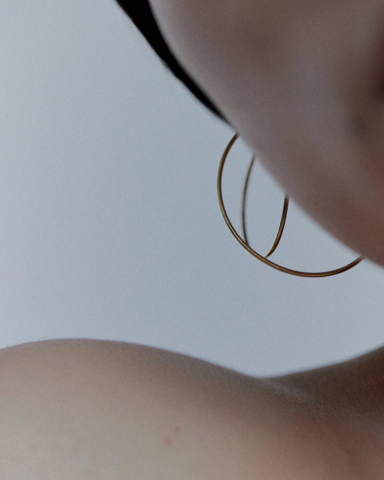Color close-up from below of single Lera Treyger Wind 14k gold thin hoop earring against soft skin