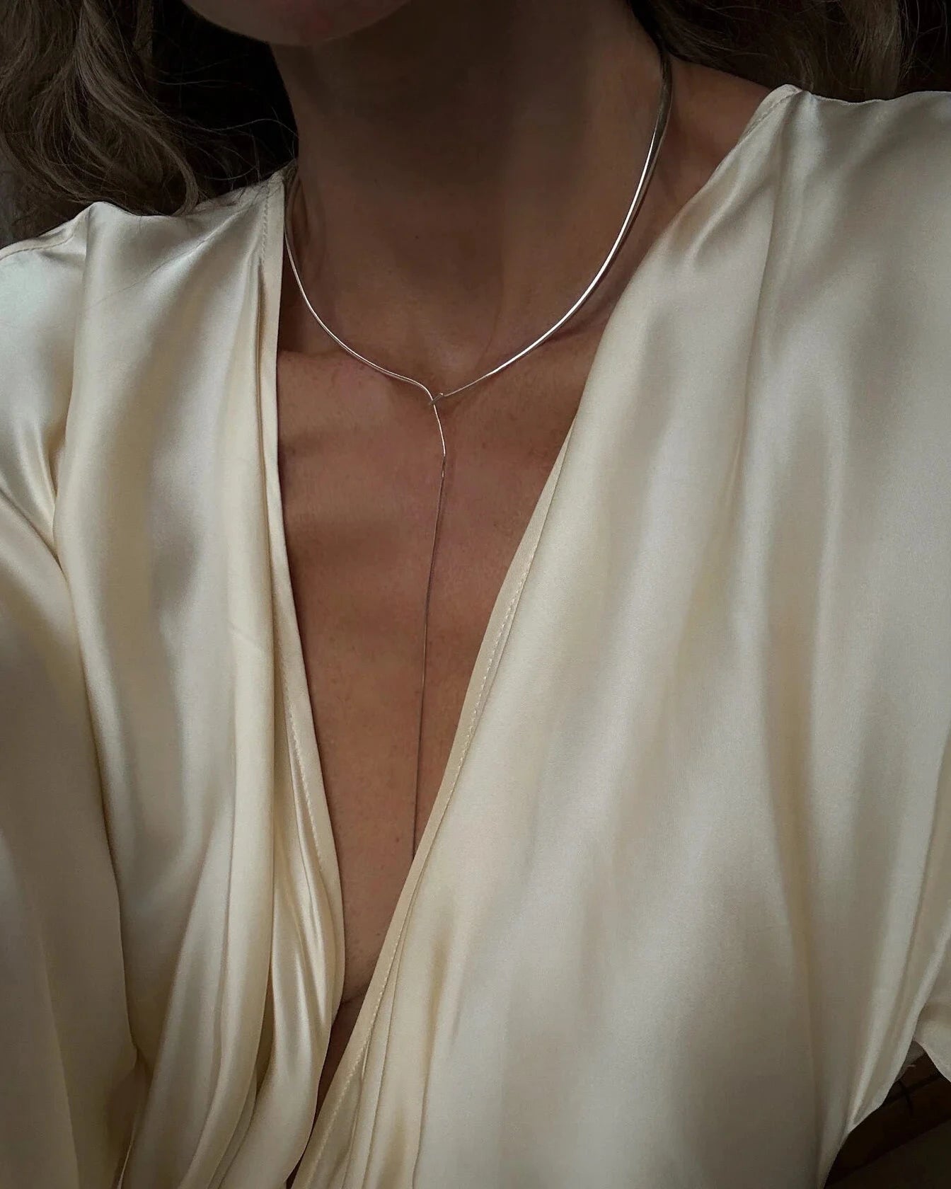 Close-up of model's chest in cream silk plunge top with Lera Treyger x Anouk Yve silver collar and lariat chain