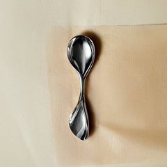Lera Treyger LOBBY sterling silver baby spoon styled flat on cream textured paper, new-life heirloom gift composition