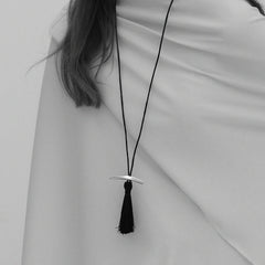 Black-and-white drape close-up of Lera Treyger Dai sterling silver curved bar pendant with black silk tassel on cord