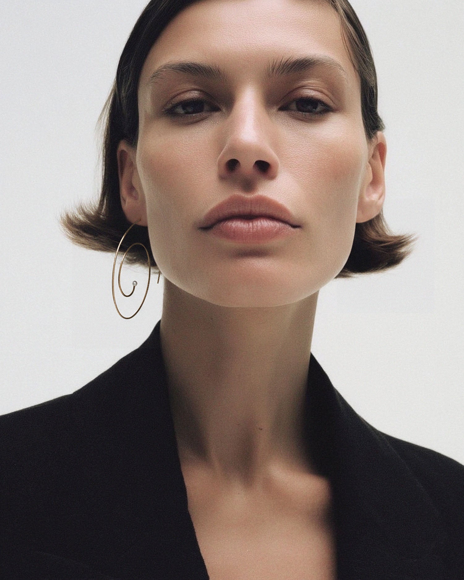 Editorial of model with short brunette bob in black blazer wearing single Lera Treyger Reisho 14k gold pearl spiral hoop