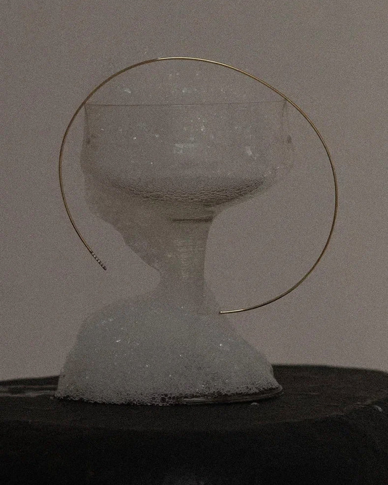 Top-down lifestyle of Lera Treyger Earth gold diamond choker arranged around a foamy champagne coupe