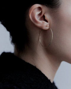 Close-up of model's ear wearing Earth m yellow gold thin medium hoop, soft natural light