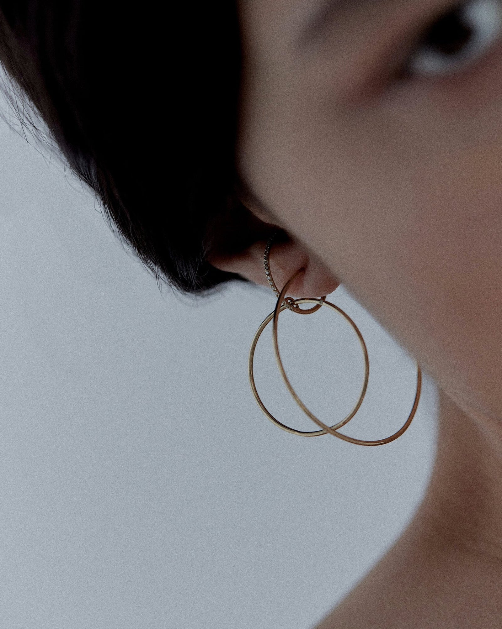 Editorial detail of Earth m gold hoop earring on model in black sweater against pale background