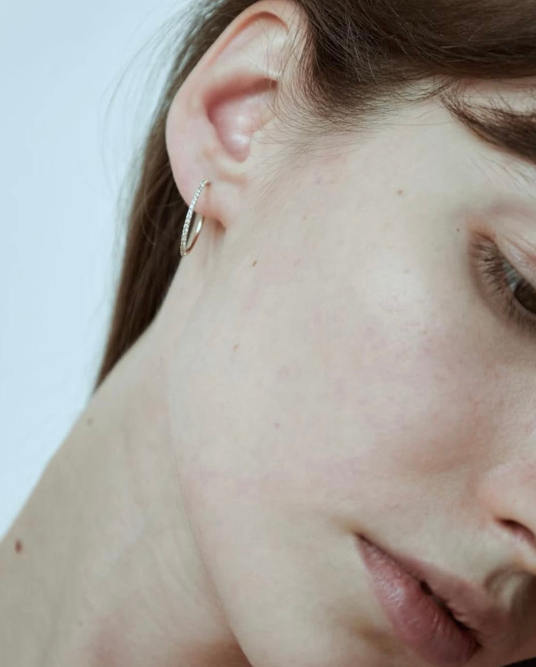Color close-up of model wearing pair of Lera Treyger Earth-S 14k gold pavé-diamond small hoops stacked in lobe