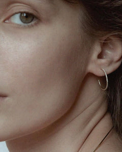 Detail of model's ear with Lera Treyger Earth-S 14k gold pavé-diamond small hoop, fine gold chain visible at neck