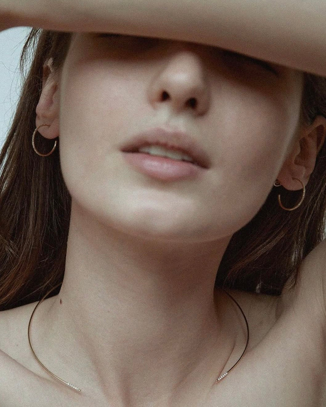 Editorial of model with arm over face wearing two Lera Treyger Earth-S 14k gold pavé-diamond hoops and fine chain
