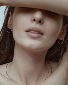 Editorial of model with arm over face wearing two Lera Treyger Earth-S 14k gold pavé-diamond hoops and fine chain