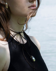 Lakeside portrait of model in black halter wearing Lera Treyger Influunt sterling silver pebble pendant on long cord with matching ear cuff