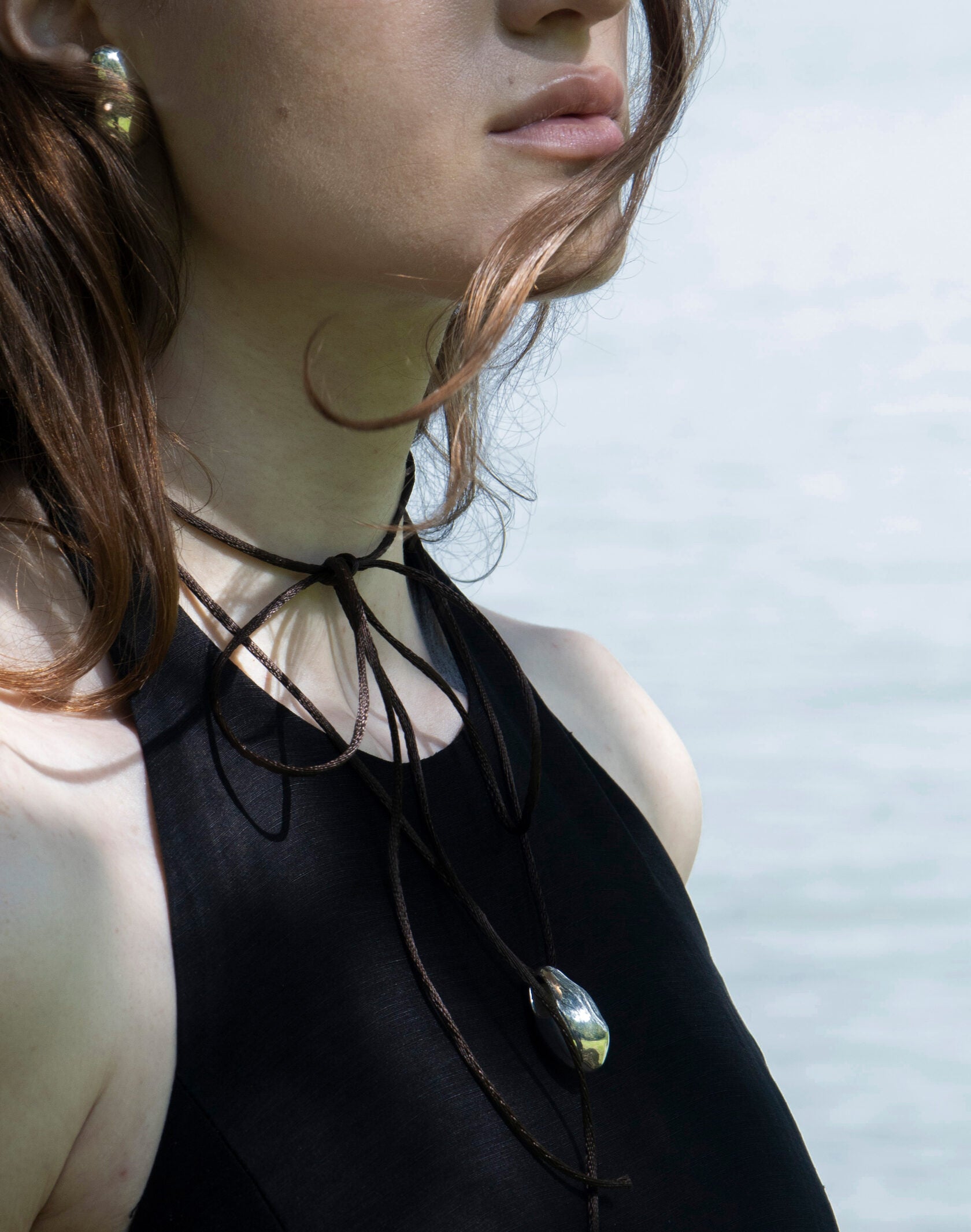 Lakeside portrait of model in black halter wearing Lera Treyger Influunt sterling silver pebble pendant on long cord with matching ear cuff