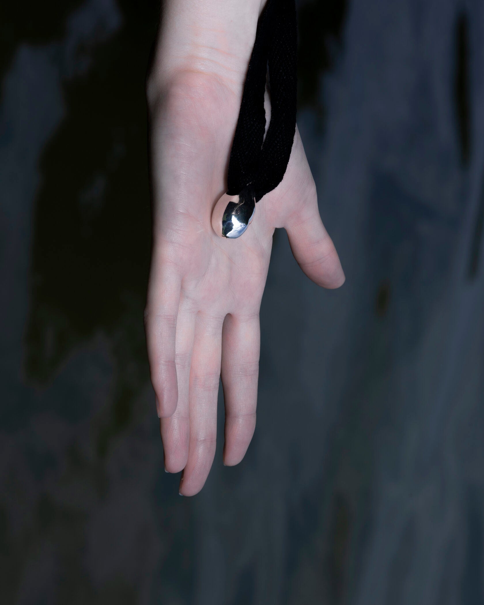 Atmospheric still life of Lera Treyger Influunt sterling silver pebble pendant resting in model's open palm against dark wall