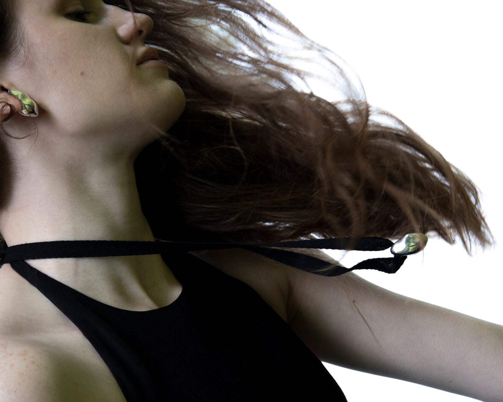 Windblown action shot of Lera Treyger Influunt sterling silver pebble pendant and matching ear cuff catching backlight