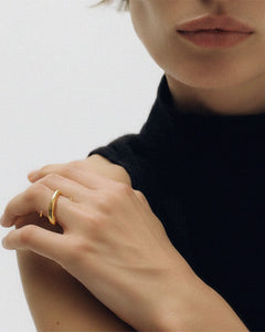 Editorial portrait of model wearing gold Kaisho ring, hand resting on shoulder against black knit