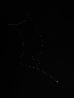 Atmospheric studio of Lera Treyger MA 9 14k yellow gold lariat traced against black background, glowing diamond drop