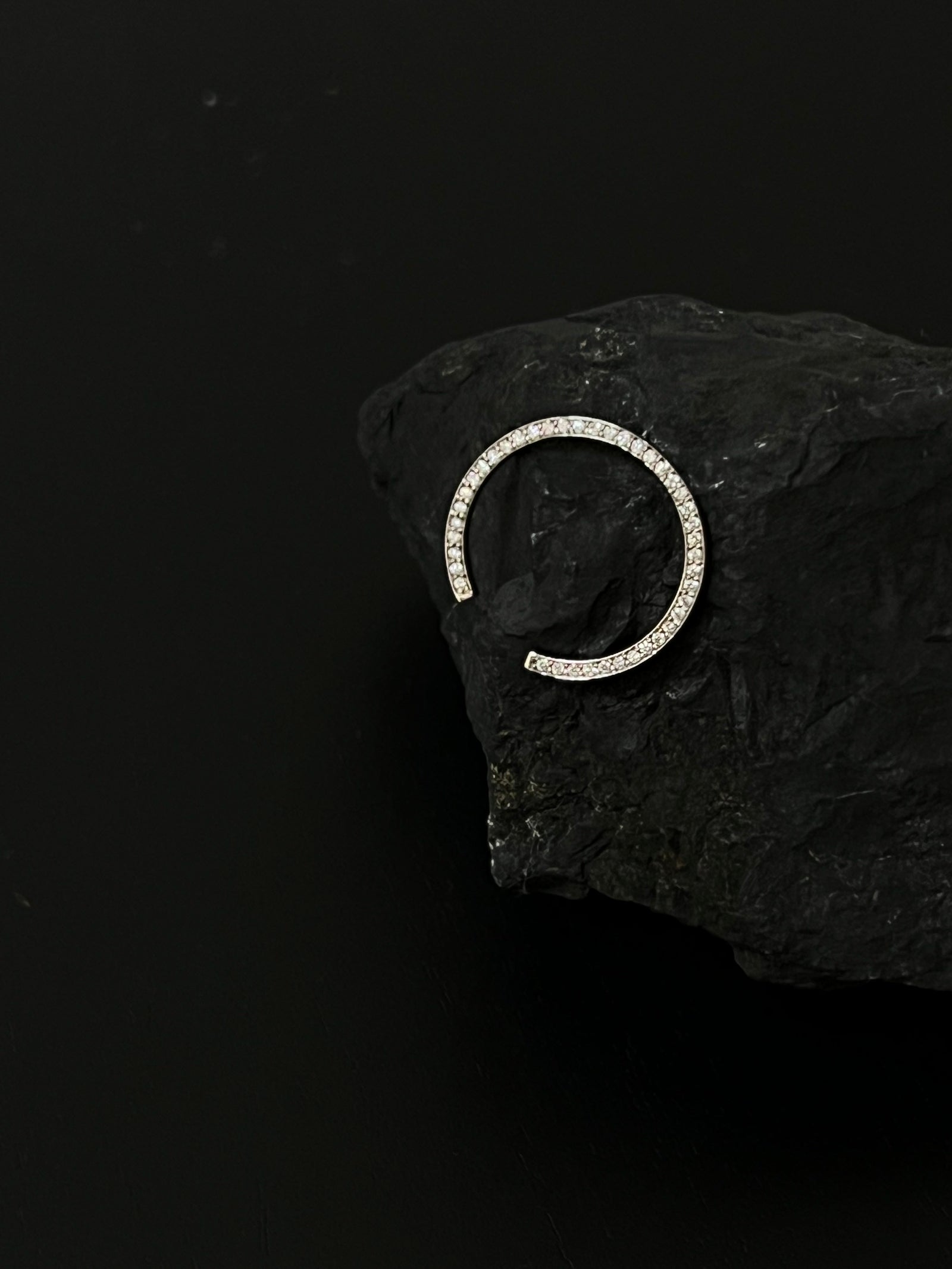 Atmospheric still life of N 14 diamond pavé ring on dark stone against black background