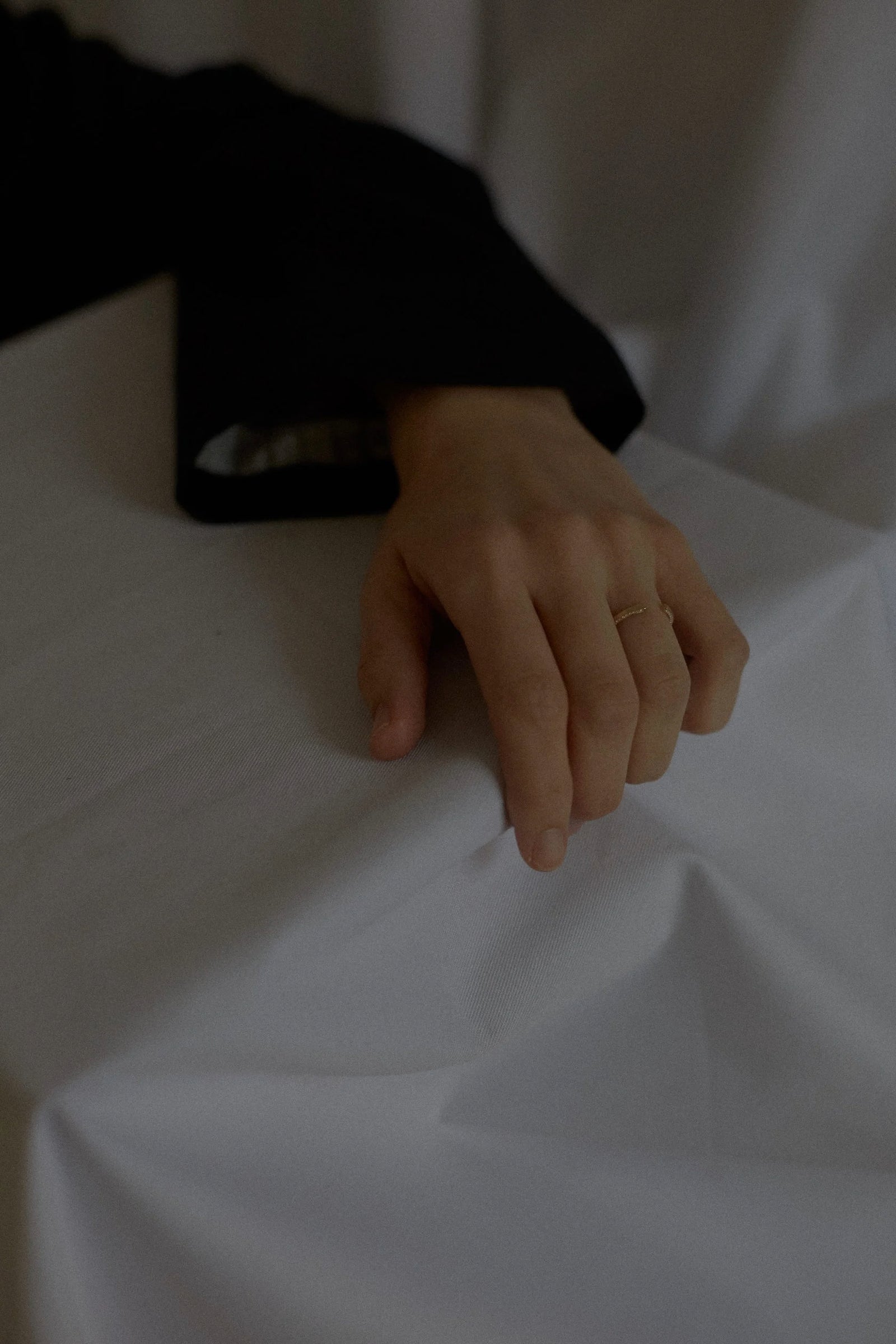 Detail of N 14 yellow gold pavé ring on hand against soft white bed sheets