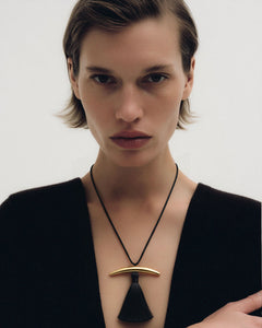 Editorial of model in deep-V black cardigan wearing Lera Treyger Dai 14k gold curved bar pendant with black silk tassel