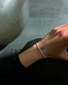 Close-up of Lera Treyger Ukiyo n 3 diamond pave tennis bracelet with emerald-cut emerald accent on hand against grey wall